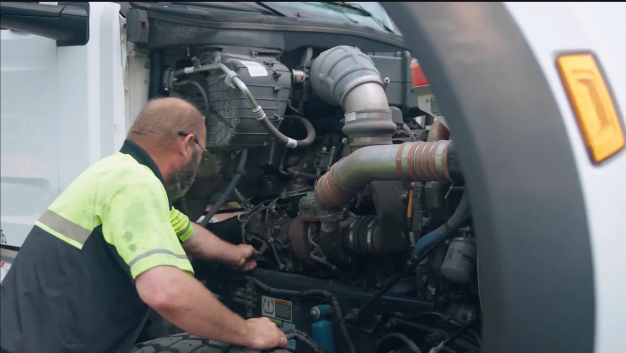 A TNA technician in a hi-vis shirt working in the open engine bay of a semi tractor