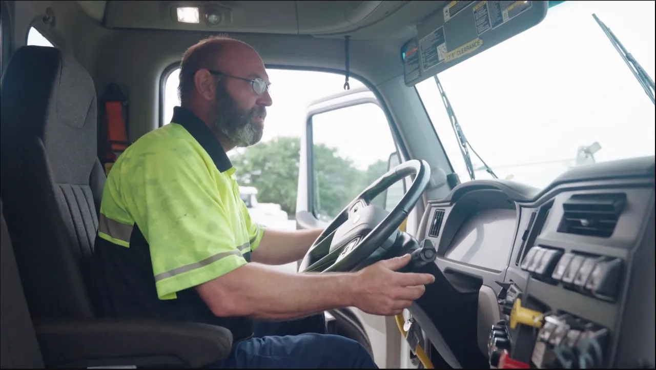 A TNA technician in a hi-vis shirt at the wheel inside a truck cab