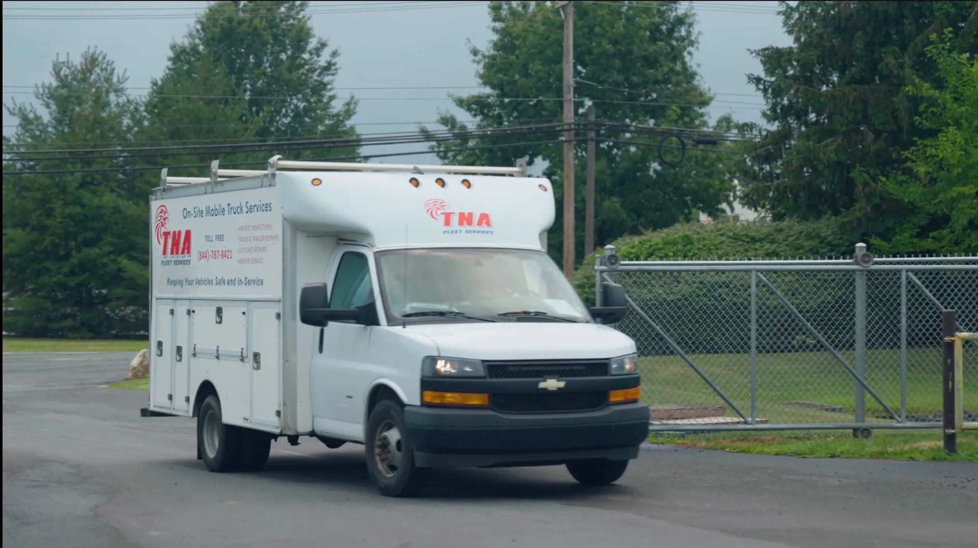 A TNA Fleet Services box truck pulling out through a yard gate